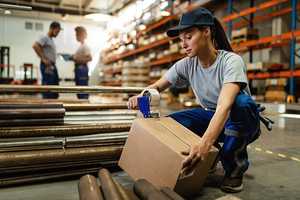 Female warehouse worker taping cardboard box with tape